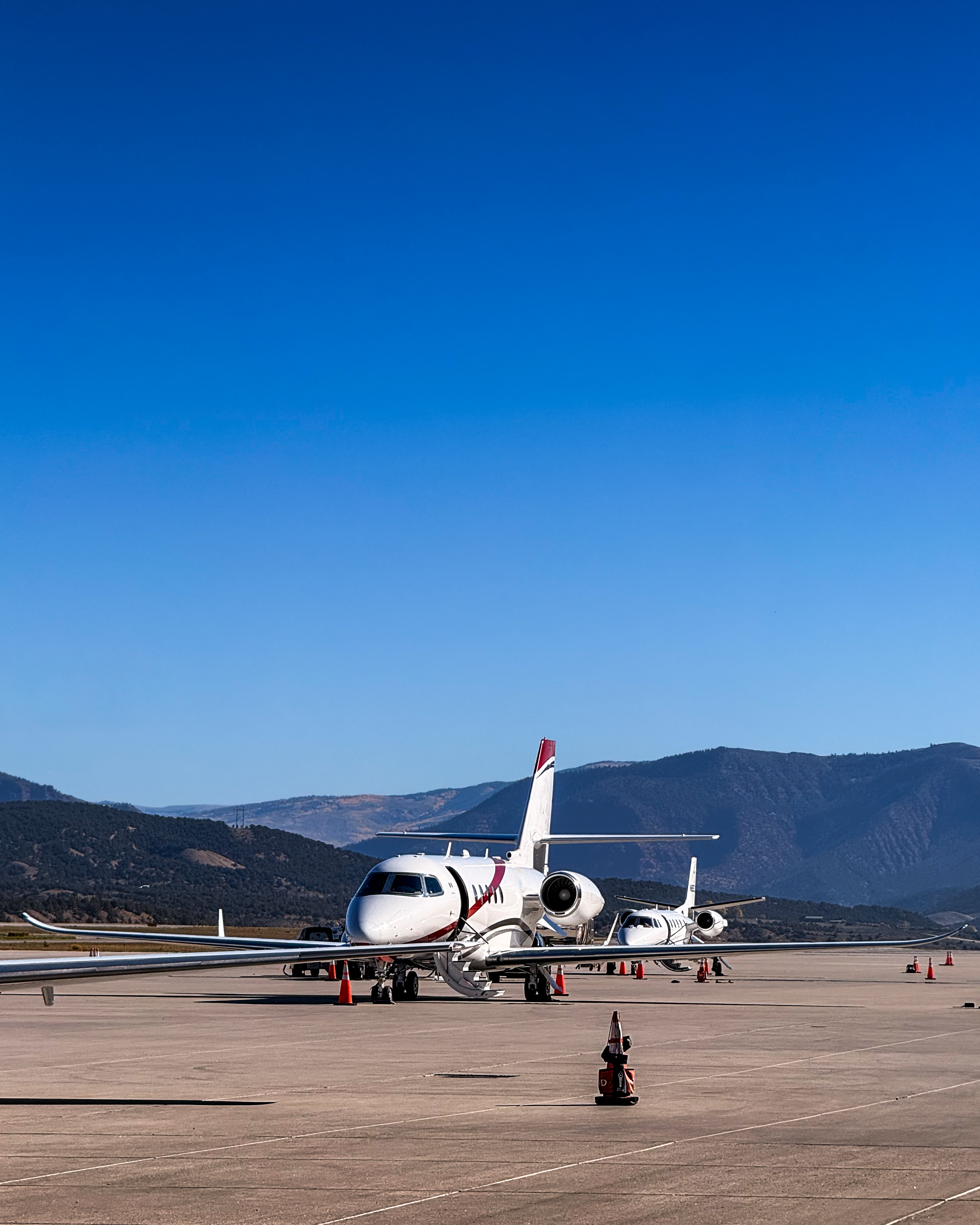 Private jets on ramp with mountain backdrop and clear blue sky